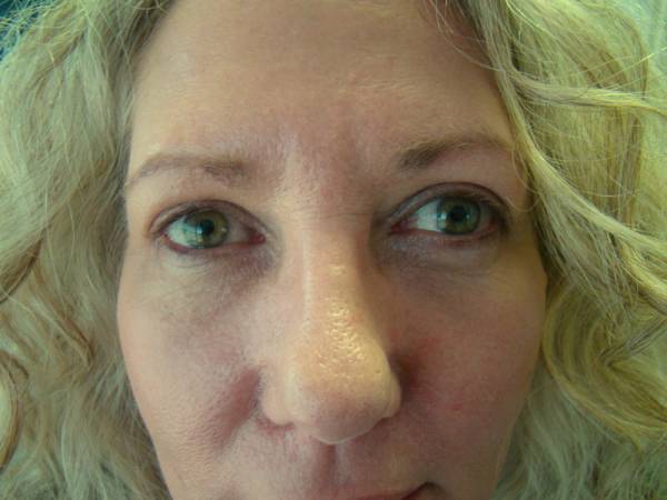 Close-up of a middle-aged woman with light skin and blonde hair, showing her face and green eyes, looking directly at the camera.