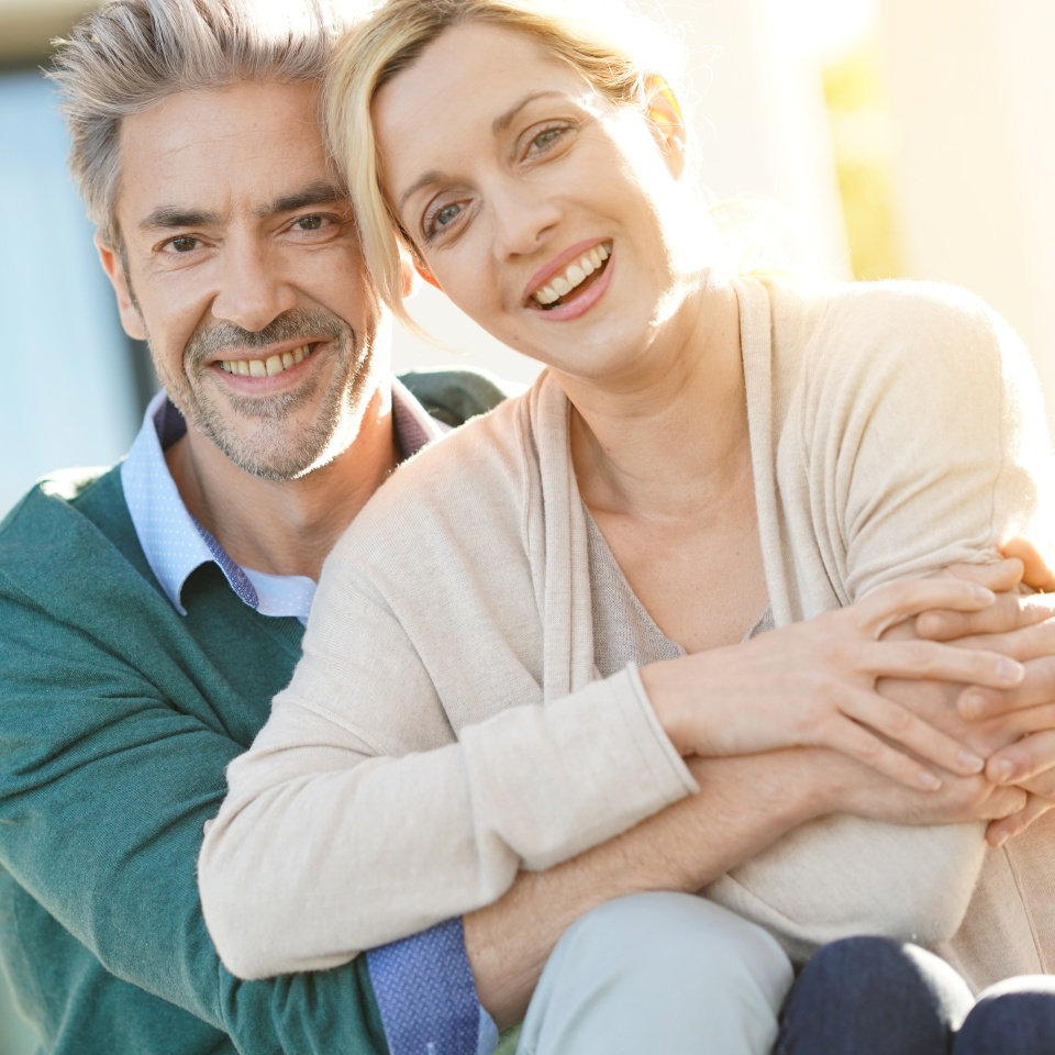 Cheerful middle-aged couple sitting in front of new home