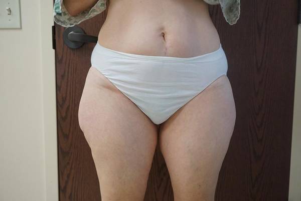 Person standing in front of a wooden door, wearing light-colored underwear, with midsection and upper legs visible.