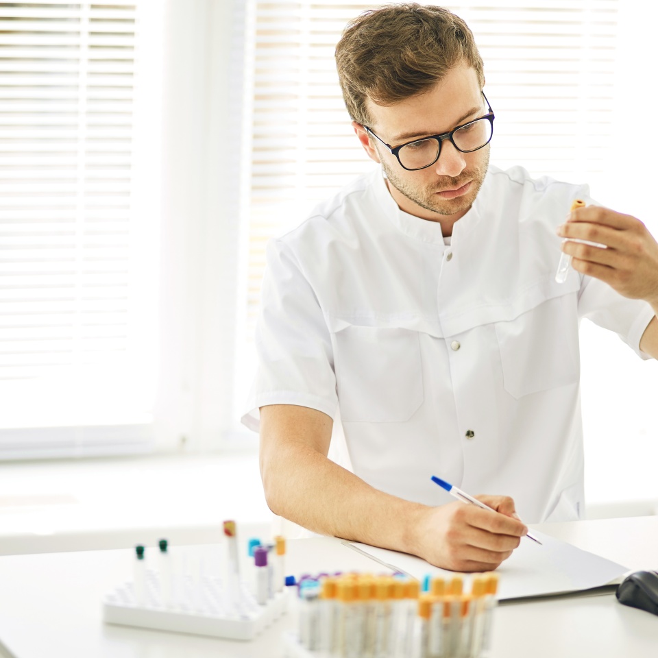 cute man is writing the results of the complete blood cell count indoors. close up photo. blood chemistry. general blood analysis. life in the tube