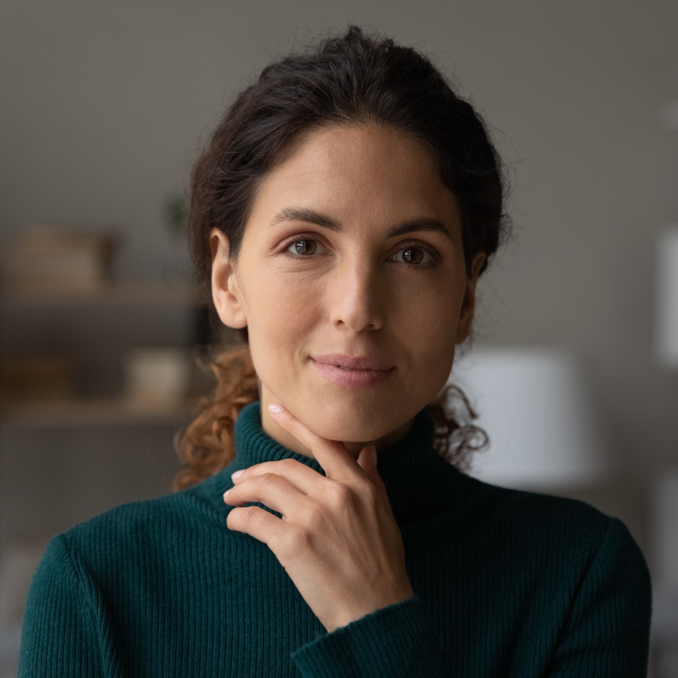 Head shot portrait beautiful calm woman touching chin, feeling self confident at home, rental tenancy concept. Happy attractive positive lady with perfect teeth and tidy hairstyle looking at camera.
