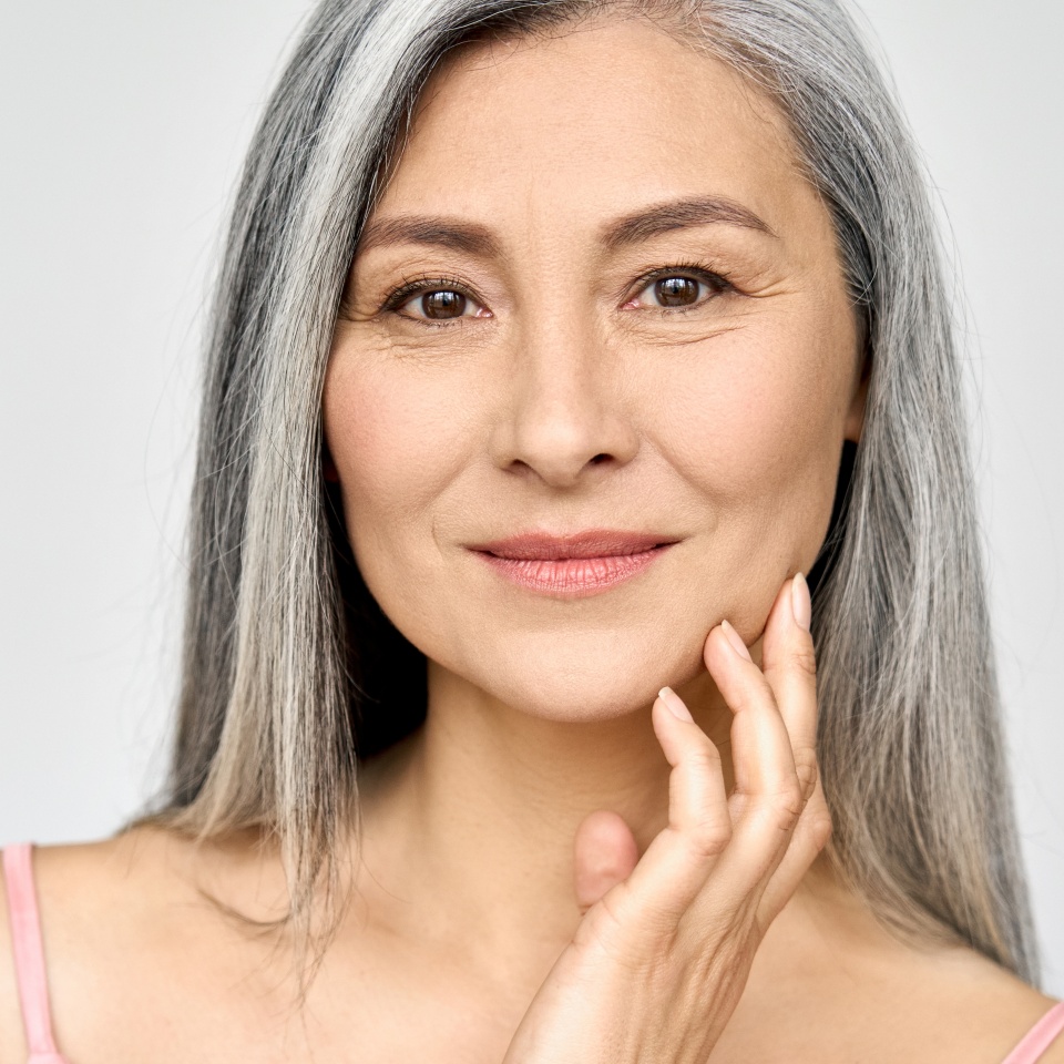 Closeup portrait of gorgeous happy middle aged mature asian woman, senior older 50 year lady looking at camera touching her face isolated on white. Ads of lifting anti wrinkle skin care treatment.