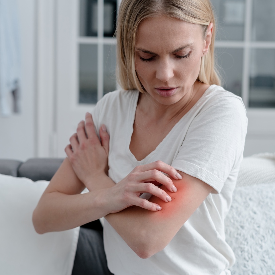 worried female feeling unwell, has allergy or reaction from insect bite, girl with itch or irritation on arm sitting on sofa in room