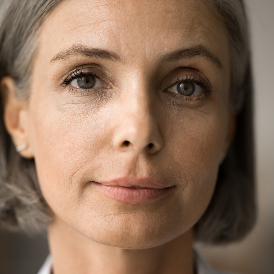 Pretty face of mature 50s grey haired woman looking at camera with positive serious calm expression. Senior lady with natural makeup promoting elderly age beauty care